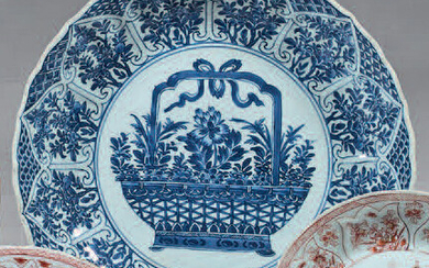 China porcelain dish. Kangxi (1662- 1722). With blue-white decoration, in the centre of a large basket of flowers in two circles, the wing and the fall of a frieze of flowering branches in cartouches, the reverse of a motif in two circles and...