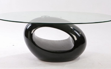 20th Century glass coffee table. the oval glass top above the black oval shaped base, 110cm long