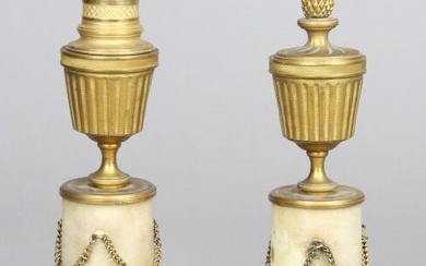 Paire de cassolettes en bronze doré et ciselé formant bougeoirs. Fûts cylindriques de marbre agrémentés...