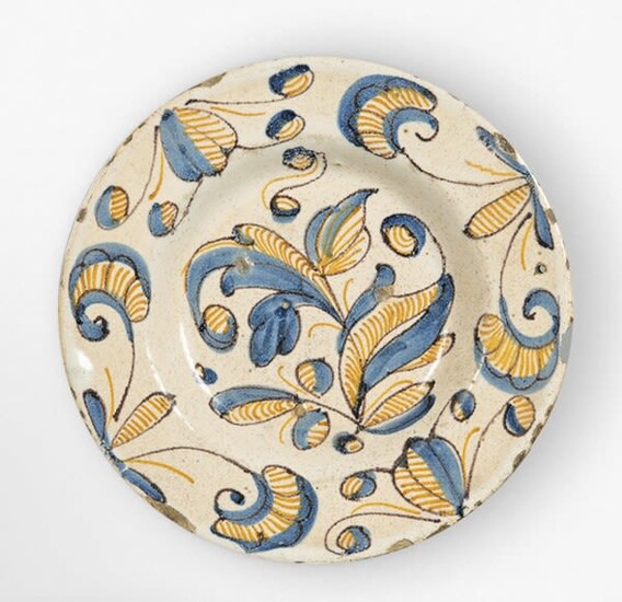 Plato de cerámica esmaltada de la serie tricolor o azul, naranja y manganeso" con una flor en el asiento y hojas en el alero.Talavera, S. XVII.