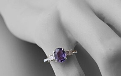 750 thousandths white gold ring centered on an oval-shaped lilac sapphire calibrating approximately 1.65 carats and set with six baguette diamonds.