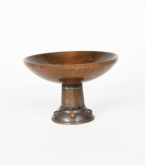 An Artificers' Guild silver, copper and wood comport probably designed by Edward Spencer, model no. 2025, the domed silver foot set with red and orange jewels, the tapering, faceted stem supporting shallow wooden bowl, stamped marks to base, 15cm...
