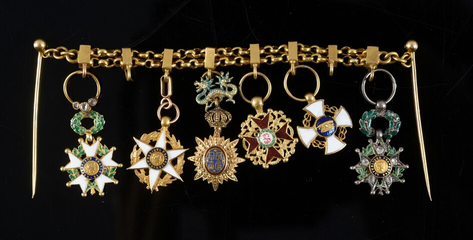 BAR FOR MINIATURE DECORATIONS. Two gold chains hold the miniature orders of the Legion of Honour with diamond roses, the Agricultural Merit, the Dragon of Annam, Saint-Stanislas, the Crown of Italy and the Legion of Honour set with diamond roses...