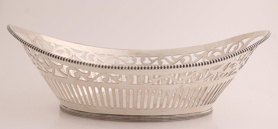 Silver bread basket, 835/000, oval sawn model with bars and floral pattern, provided with a soldered pearl rim. Placed on an oval ring with fillet edge, dent in. MT .: J. Krins, Schoonhoven, jl.:g:1966. about 335 grams. 27x18x9cm. In good condition