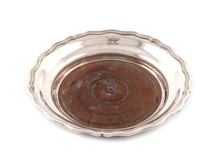 A 19th century Colonial silver wine coaster, marked with pseudo English marks and maker~s mark JS script, unidentified, shallow circular form, moulded border, and engraved with a crest, wooden base, diameter 17.8cm.