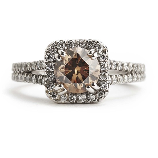A diamond ring set with a brilliant-cut fancy cognac coloured diamond encircled and flanked by numerous brilliant-cut white diamonds, mounted in 14k white gold.