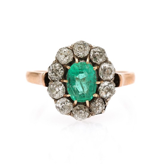 An emerald and diamond ring set with an oval-cut emerald encircled by ten old-cut diamonds, mounted in 18k rose gold and silver. Size 52.5.