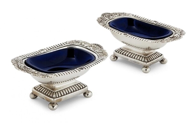 A pair of George III silver salts, London, c.1809, Rebecca Emes & Edward Barnard I, designed with shell and foliate decoration to shaped rectangular rims, each with blue glass liner and raised on four ball feet, gilded interiors (one faded) 12.1cm...