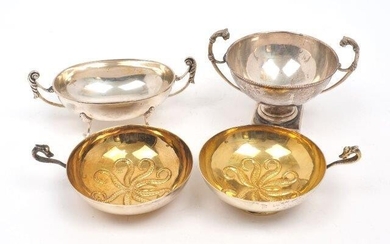 Two continental gilt drinking cups with zoomorphic handles, stamped 900, each with repousse octopus design to base, 10.9cm dia., together with two twin handled white metal dishes, one oval (16cm long inc. handles), one circular (13.8cm wide inc...