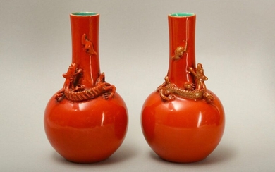 A PAIR OF SALMON RED-GLAZED 'DRAGON' VASES. Qing Dynasty. The globular body of each bottle-shaped vase supporting a well modelled qi dragon coiled in mirror image and looking up at a back modelled to the slightly tapered long cylindrical neck, each...