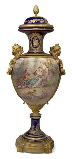A large gilt-bronze mounted Sevres style baluster vase and cover, 19th Century, in gilt and navy blue colour ways decorated to the body with a pastoral scene, the ormolu mounts as cherub masks with rose garlands, the cover with acorn finial, 79cm...