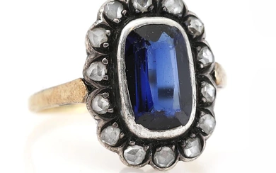 A sapphire and diamond ring set with a synthetic fancy-cut sapphire encircled...