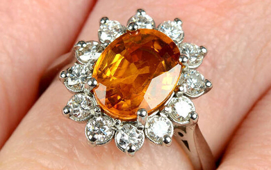 An orange sapphire and brilliant-cut diamond cluster ring.