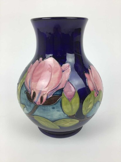 Moorcroft pottery vase decorated in the Magnolia pattern on blue ground, impressed marks and green painted signature to base, 25cm high