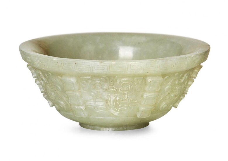 Property of a Gentleman (lots 36-85) A small Chinese green jade archaistic bowl, 18th century, finely carved with taotie masks interspersed with six rows of three ingot-shaped flanges, 8cm diameter, later hardwood stand