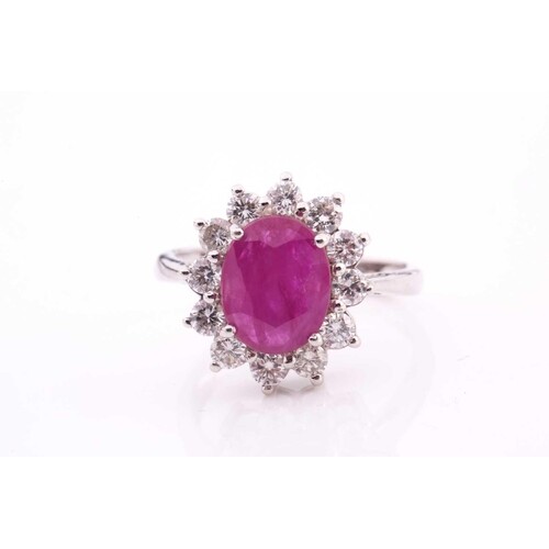 A ruby and diamond cluster ring, set with an oval ruby measu...