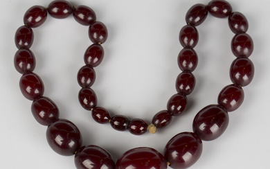 A single row necklace of graduated oval dark cherry coloured reconstituted amber beads on a threaded