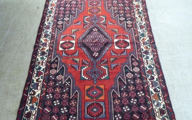 A Persian rug, decorated with stylised designs, on a red gro...