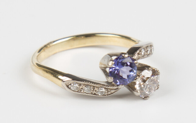 A gold, tanzanite and diamond ring in a crossover design, claw set with a circular cut diamond and a