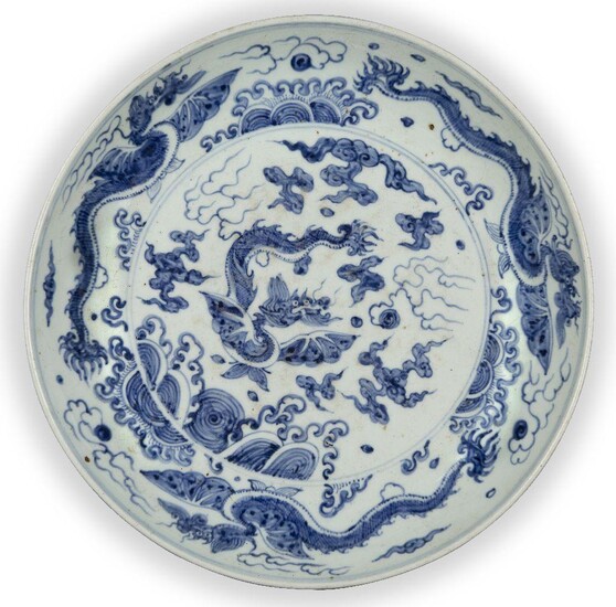 A large Chinese porcelain blue and white 'dragon' dish, late Qing dynasty, painted to the central reserve with a winged dragon above crashing waves amidst cloud swirls and flames inside a border decorated with three dragons, 33cm diameter