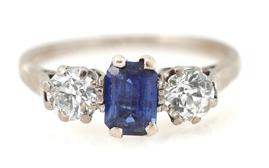 A sapphire and diamond ring set with an emerald-cut sapphire flanked by...