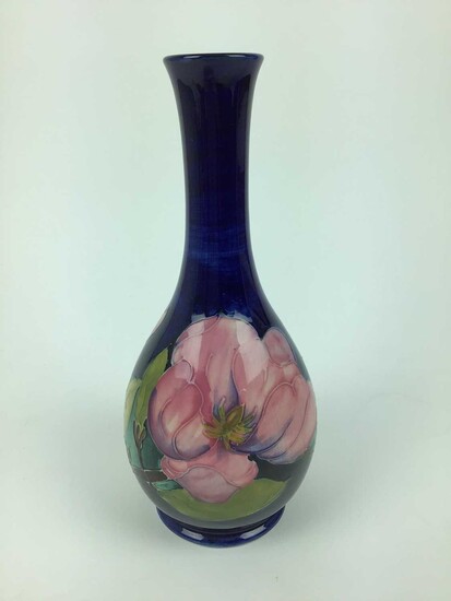 Moorcroft pottery slender neck vase decorated in the Magnolia pattern on blue ground, impressed marks and green painted signature to base, 27cm high