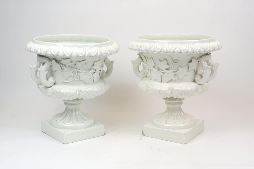 A pair of Continental white glazed pottery twin handled campana urns, 20th century, the bodies with trailing ivy moulded in relief and on fluted socles, printed mark to the underside, each 32cm high (2)