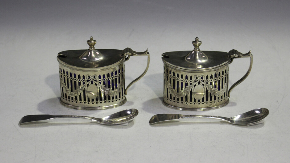 A pair of Edwardian silver oval mustards, each with hinged lid and urn shaped finial above pierced a