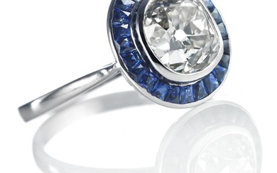 A sapphire and diamond ring in Art Deco style set with an old mine-cut diamond weighing app. 3.01 ct. encircled by numerous fancy-cut sapphires, mounted in platinum. Colour: Top Crystal (I). Clarity: VVS. Size 56.5. London 1999, England.