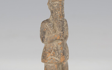 An ancient terracotta figure, probably Sumerian, modelled with his hands clasping his long beard, le