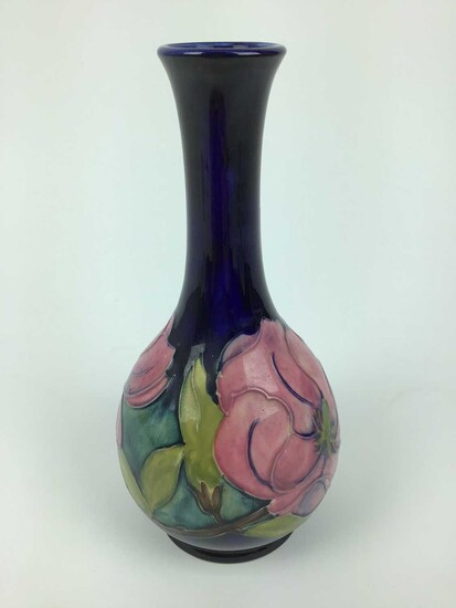 Moorcroft pottery slender neck vase decorated in the Magnolia pattern on blue ground, green painted signature to base, 21.5cm high