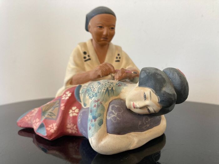 Okimono - Terracotta - Hakata Doll sculpture with a man tattooing a dragon on a bijin 美人 (beauty) - Japan - ca 1960s (Showa period)