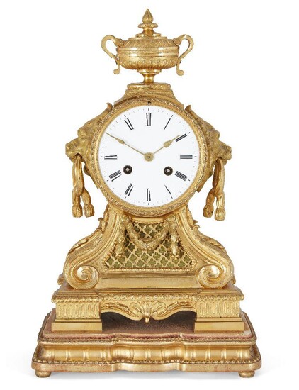 A French gilt-bronze mantle clock, 19th century, the ormolu case surmounted by a twin handled urn, having twin lion mask and tassel handles, on scrolling supports with pierced quatrefoil panels, on stepped plinth base, the white enamel dial with...