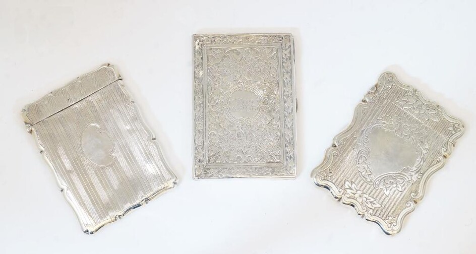A group of three silver card cases, comprising: a Victorian example, Birmingham, 1876, probably Hilliard & Thomason, marks rubbed, with vine leaf decoration and central cartouche with engraved monogram, with lined interior, 9.6cm high, 6.9cm wide;...