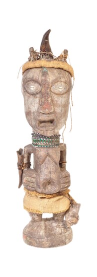 A large 20th Century tribal African figure with horn set to head with inset shells to eyes. Glass bead necklaces with cloth skirt raised on pedestal base. Measures approx; 80cm tall.