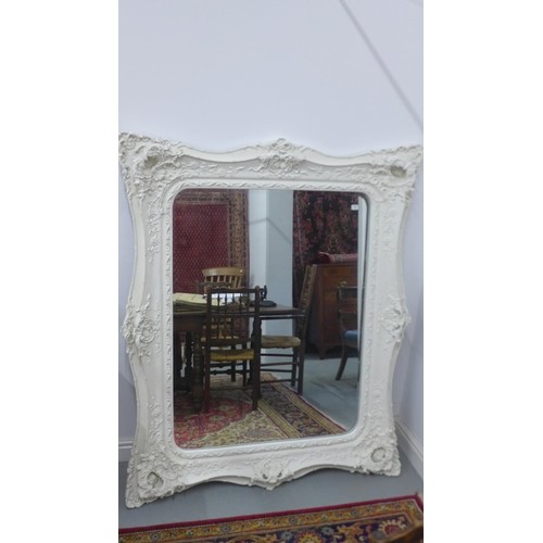 A large white ornamental framed mirror with bevelled glass p...