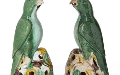 A pair of Chinese green-glazed biscuit porcelain parrots, Kangxi period, modelled standing on pierced brown, yellow and green rockwork bases, 18cm high, on fitted carved wood stands (2) Provenance: Private French collection