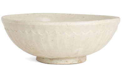 A Chinese stoneware white-glazed 'lotus' bowl, Northern Song dynasty, on a short, slightly flared foot with rounded sides, the exterior moulded with a band of continuous lotus petals, covered in white slip under a clear glaze that falls just short...