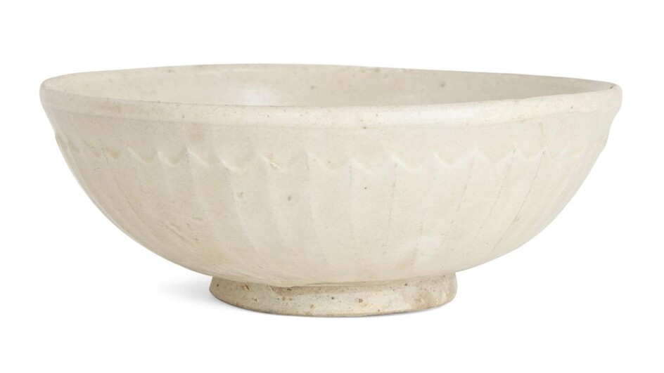 A Chinese stoneware white-glazed 'lotus' bowl, Northern Song dynasty, on a short, slightly flared foot with rounded sides, the exterior moulded with a band of continuous lotus petals, covered in white slip under a clear glaze that falls just short...