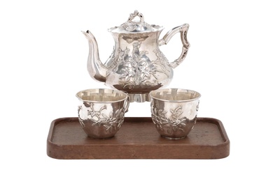 A set of a silver teapot and two cups with relief decor of flowers and a bird. The cups on a wooden tray. Marked with two seal marks, including TianJin BaoCheng. China, around 1900. H. 6 - 13 cm. Total weight (silver) approx. 560 g.