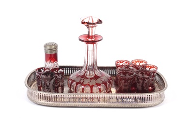 A Bohemian engraved ruby flashed decanter and matched glasses on a tray. The decanter engraved with fruiting vinea, with nine matched engraved shot glasses in differing shapes and a salt shaker similar, the silver-plated shaped rectangular galleried...