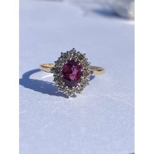 A ruby and diamond ring, of cluster design, set with an oval...