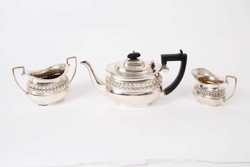 George V silver three piece bachelor's tea set, comprising teapot of compressed baluster form, with angular ebony handle and hinged domed cover, matching sugar and milk jug, (Chester 1912)