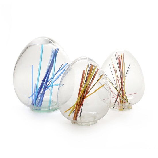 Monica Backström: Three clear glass objects in the shape of eggs, inlaid with “sticks” of blue, orange, yellow, black and white glass. (3)