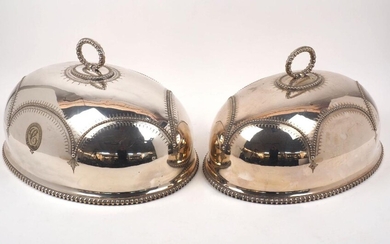 Two silver plated domed dish covers, of oval form with loop handles and gadrooned rims, designed with scalloped beading to bodies and engraved with monograms and patterned banding, the larger example 51cm long, the smaller example 46cm long (2)