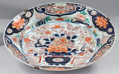 Large Japanese porcelain dish (Arita). 17th century, circa 1680. Imari decoration, in the center of a vase of flowers in front of a hedge with birds in a medallion, the wing and the fall of a frieze of mantling with flowers and butterflies, the...