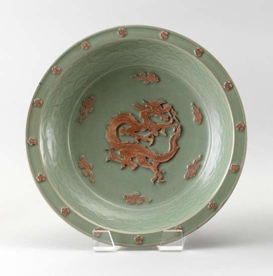 CHINESE LONGQUAN CELADON PORCELAIN SHALLOW BOWL Raised unglazed decoration of a dragon amidst fiery pearls surrounded by a wave inne...