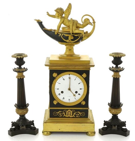 Empire clock in bronze and metal, in green and gold tones, surmounted by a cherub with an oil lamp, enamelled dial marked "à Paris". The clock is accompanied by a pair of torches. H 46.5 cm (clock), H 29 cm (torches). Non-blocked mechanism, pendulum...