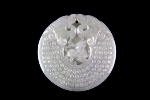 A Chinese carved pale celadon jadeite jade pendant of a coiled dragon with a dragon in the centre, Dia. 5cm.