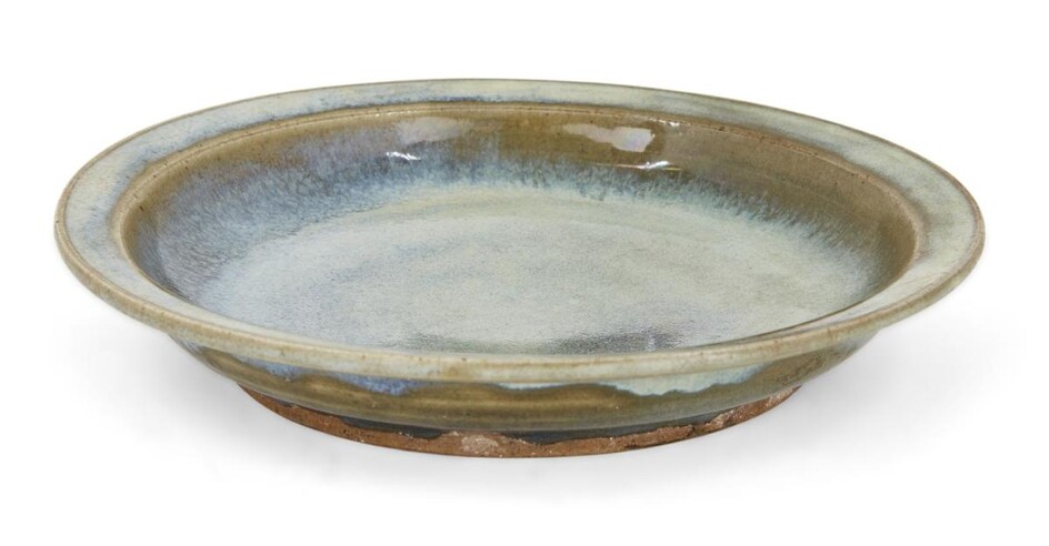 A Chinese Jun ware dish, late Ming dynasty, on a short wide foot with shallow sides that rise to an everted rim, covered in a pale blue glaze with speckles of lavender that thins to a light brown tone at the rim and cavetto, 17cm diameter